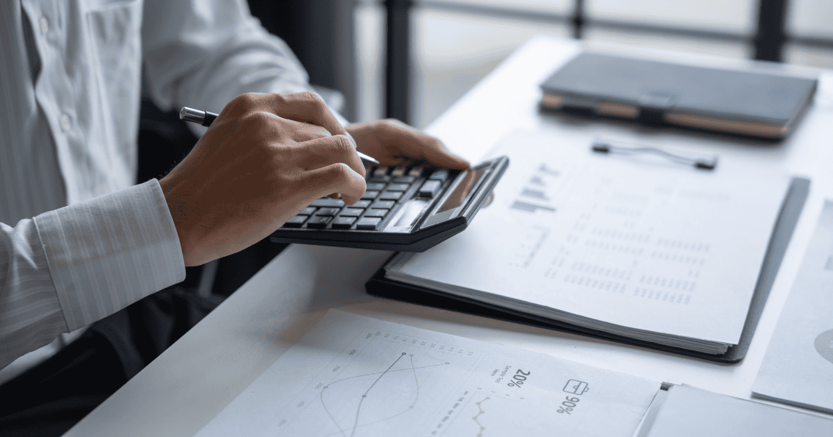 Person using calculator with financial documents and laptop on desk. Financing.